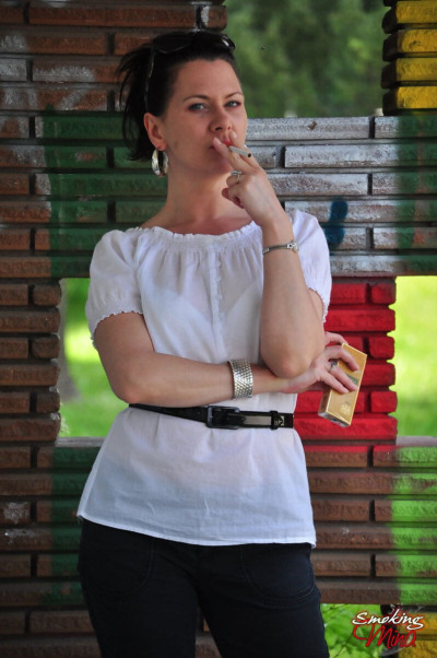 पूरी तरह से कपड़े के साथ काले बाल वाली मीना धूम्रपान करता है एक सिगरेट में सामने के एक ईंट दीवार