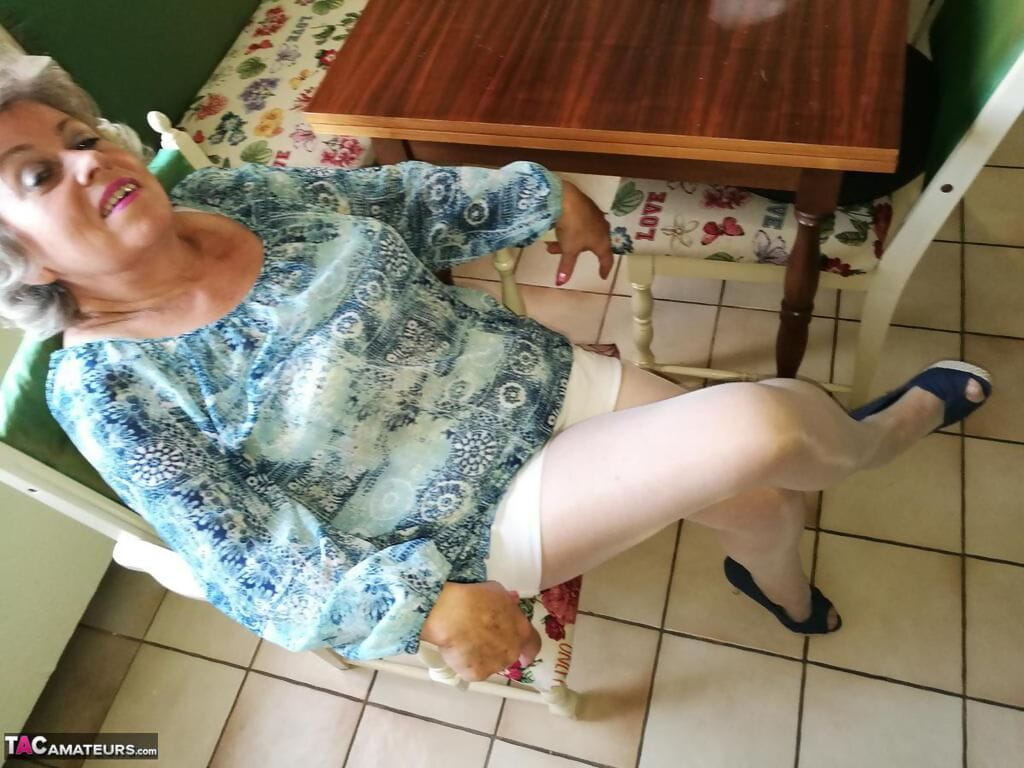 Old woman Caro pulls down her pantyhose in high heels at kitchen table page 1