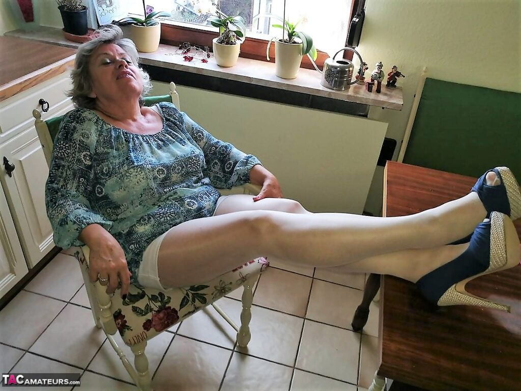 Old woman Caro pulls down her pantyhose in high heels at kitchen table page 1